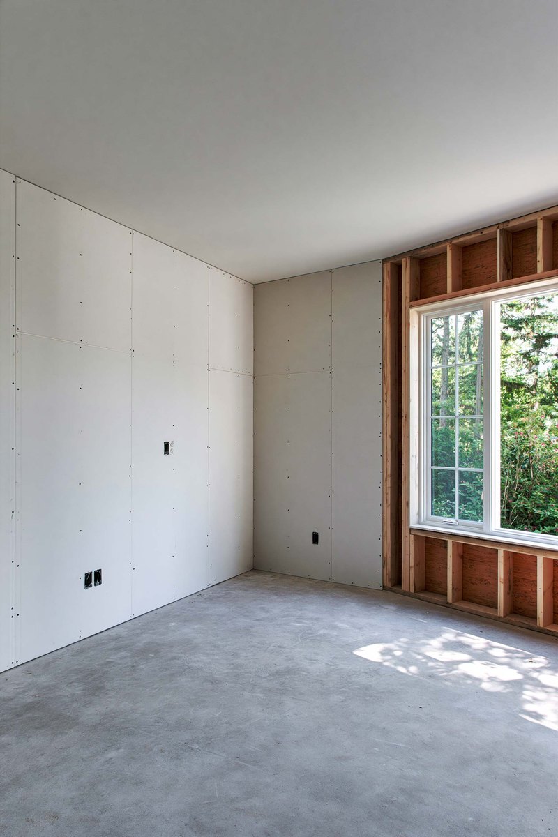 New drywall screwed to the studs with the joints still open, bare framing beside a window